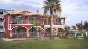 A two-story building with a red facade, balconies, and a palm tree in the front yard. - Casa Maria (Zakynthos)