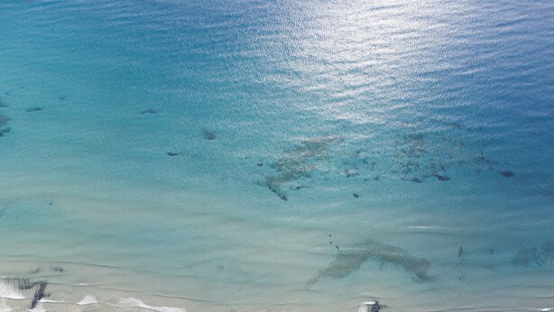 An aerial view of a beach with clear turquoise waters, a sandy shore, and a few buildings in the distance. - Casa Maria (Zakynthos)