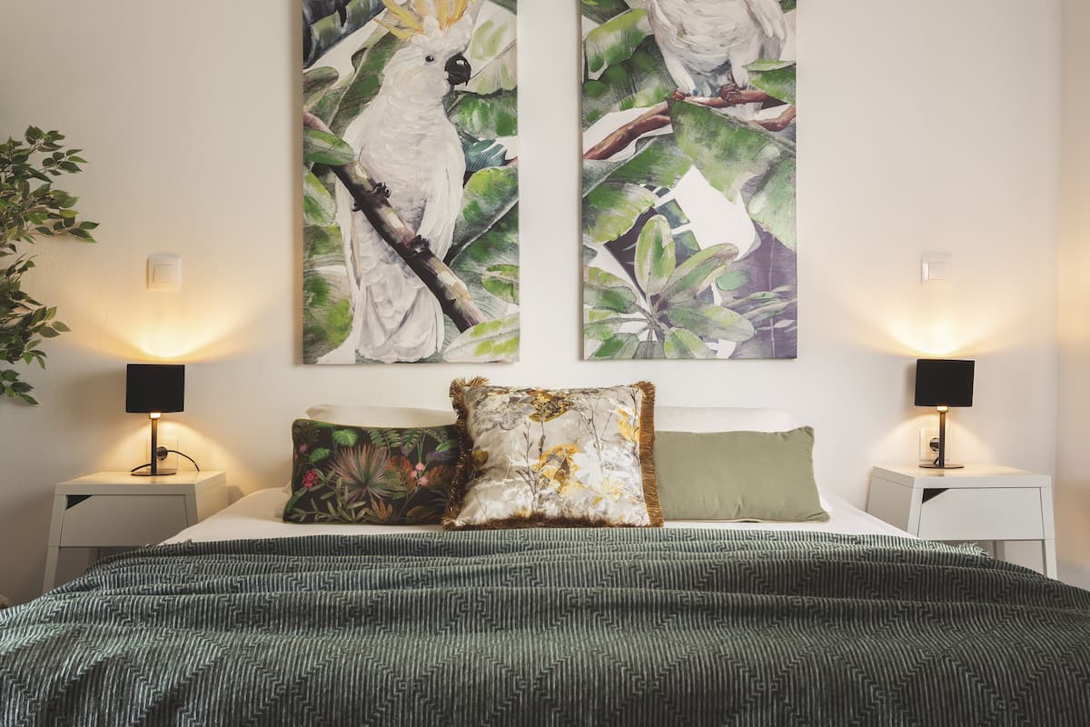 Een slaapkamer met een bed, twee nachtkastjes, twee wandlampen en twee schilderijen van vogels.