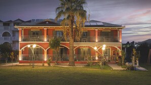 A two-story hotel with a balcony on each floor, a palm tree in the front yard, and a well-lit entrance. - Casa Maria (Zakynthos)