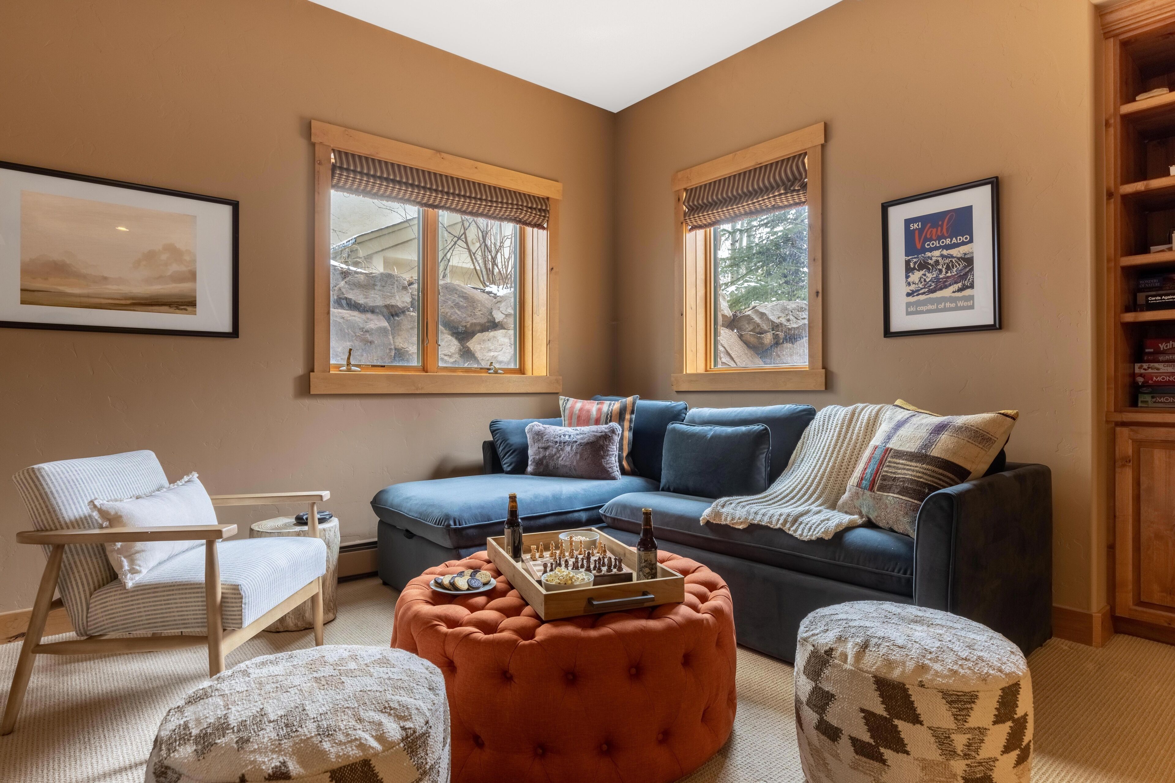 A cozy living room with a blue sofa, a wooden coffee table with chess pieces, and a patterned ottoman.