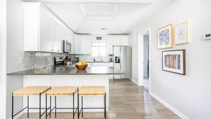 Een moderne keuken met witte kasten, een centraal eiland met krukken en een spatwand.