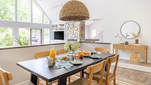 Een eetgedeelte met een donker houten tafel, een rotan hanglamp en stoelen. Een stenen muur en ramen zorgen voor daglicht.