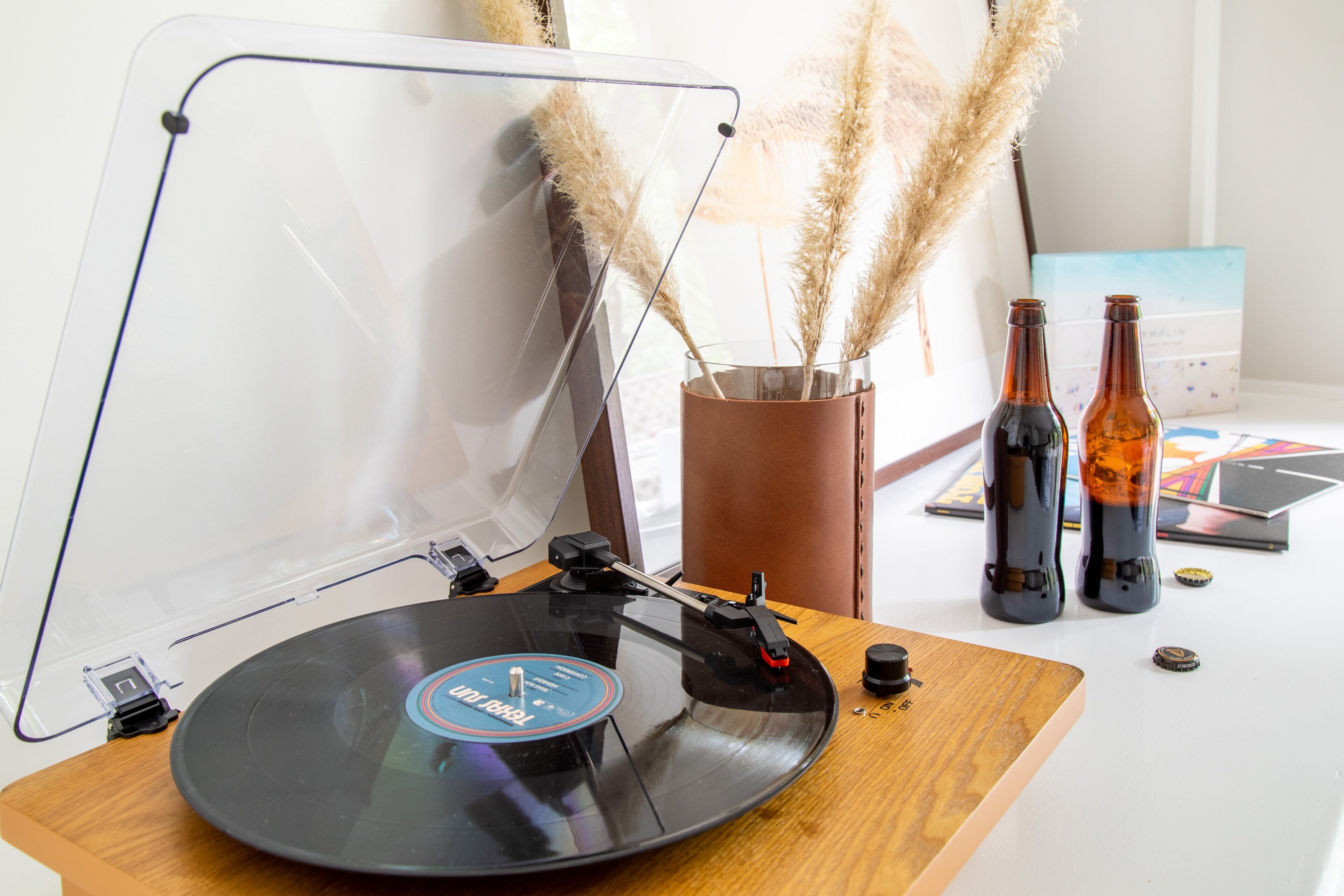 A turntable with a vinyl record, two bottles, and pampas grass in a vase on a table.