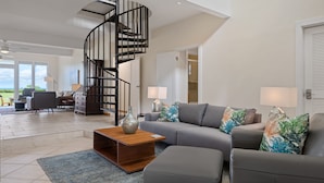 Un salon spacieux doté d’un escalier moderne, d’un canapé gris et offrant une vue sur l’extérieur.