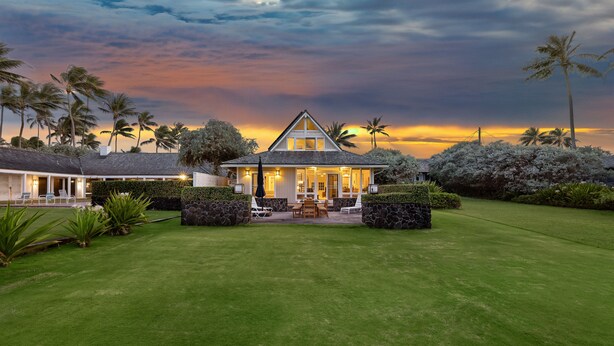 Une maison avec une pelouse bien entretenue, une terrasse avec des sièges et une vue sur le coucher de soleil.