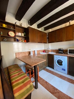 Cuina compacta amb armaris de fusta, rentadora integrada, un rentaplat i una banca amb coixí a ratlles.