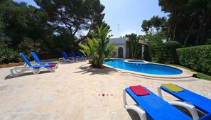 A pool area with blue lounge chairs, a small pool, and a building in the background.
