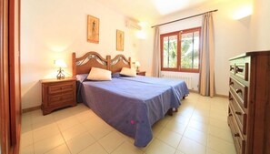 A bedroom with a double bed, two bedside tables with lamps, a dresser, and a window with curtains.