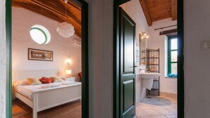 Une chambre à coucher avec un lit, une table de chevet et un tableau accroché au mur. Il y a une salle de bain avec un lavabo, un miroir et un porte-serviettes.