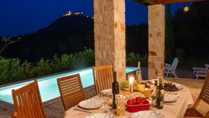 Un espace extérieur aménagé pour les repas, avec vue sur la piscine, des piliers en pierre et des chaises en bois.