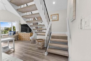 Un vaste espace de vie comprenant un escalier, un canapé, un téléviseur et une vue sur l’extérieur.