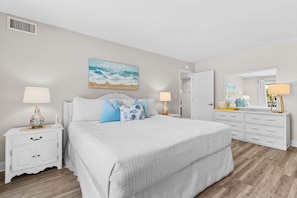 A bedroom with a large bed, two bedside tables with lamps, a dresser, and a painting on the wall.