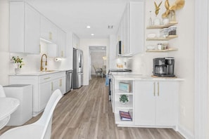 A modern kitchen with white cabinetry, a wooden floor, and a coffee machine.