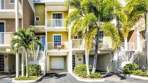 A multi-story residential building with balconies, a garage, and palm trees.