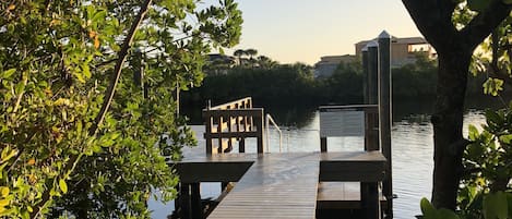 A wooden dock extending into calm water, surrounded by lush greenery and trees.