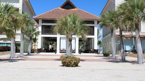 Un hôtel avec un toit recouvert de tuiles, des palmiers et un parterre de fleurs au centre.