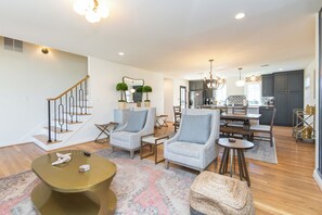A modern living room with a staircase, a dining area, and a kitchen.