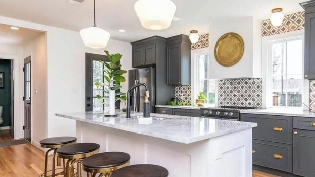 Una cocina moderna con una isla central, taburetes de bar, armarios oscuros y un salpicadero con diseño.
