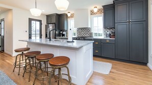 Una cocina moderna con una isla grande, taburetes de bar, armarios oscuros e iluminación colgante.