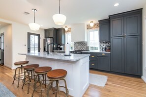 A modern kitchen with a large island, bar stools, dark cabinetry, and pendant lighting.