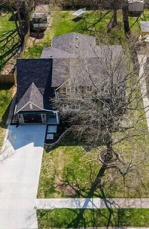 An aerial view of a residential area with a house featuring a sloped roof, a garage, and a yard with a tree.