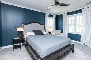 A bedroom with a bed, a nightstand, a chair, a ceiling fan, and a window with curtains.