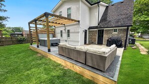 Un patio trasero con jacuzzi, mobiliario exterior y una pérgola.