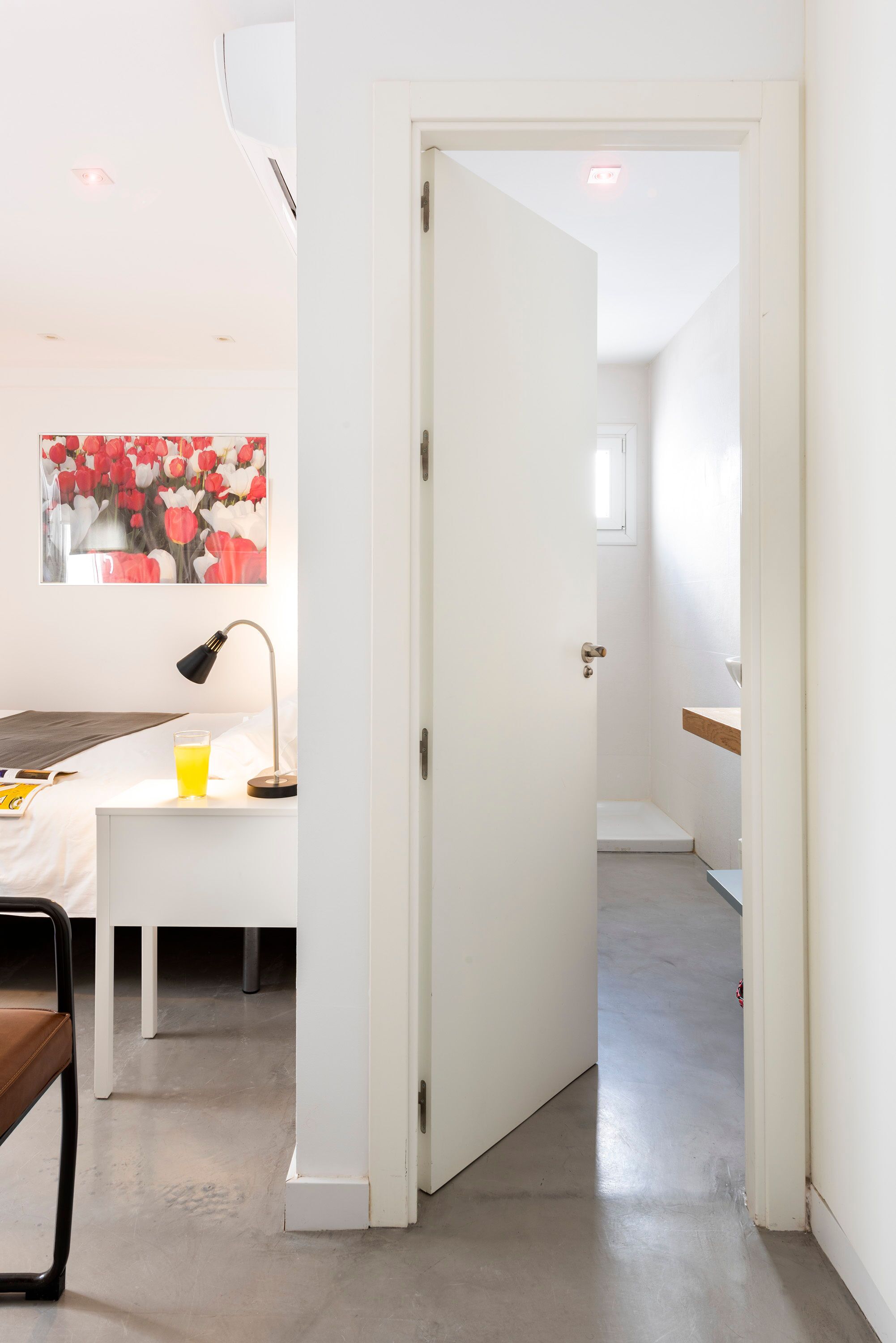 Een moderne hotelkamer met een bed, nachtkastje, lamp en een schilderij aan de muur.