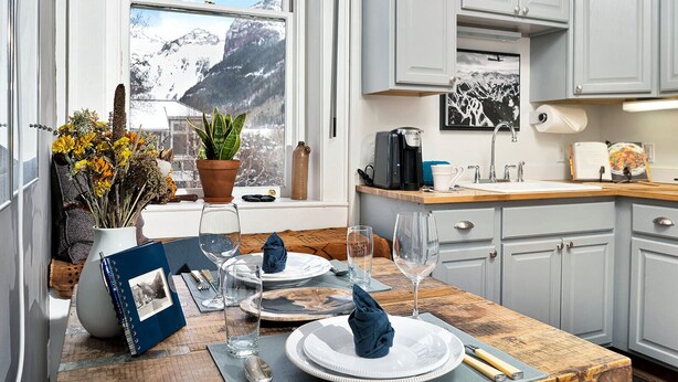 A modern kitchen with white cabinets, a wooden countertop, and a view of snow-capped mountains through a large window.