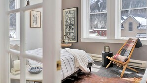 A bedroom with a bed, a chair, a radiator, and a window with a view of a snowy landscape.
