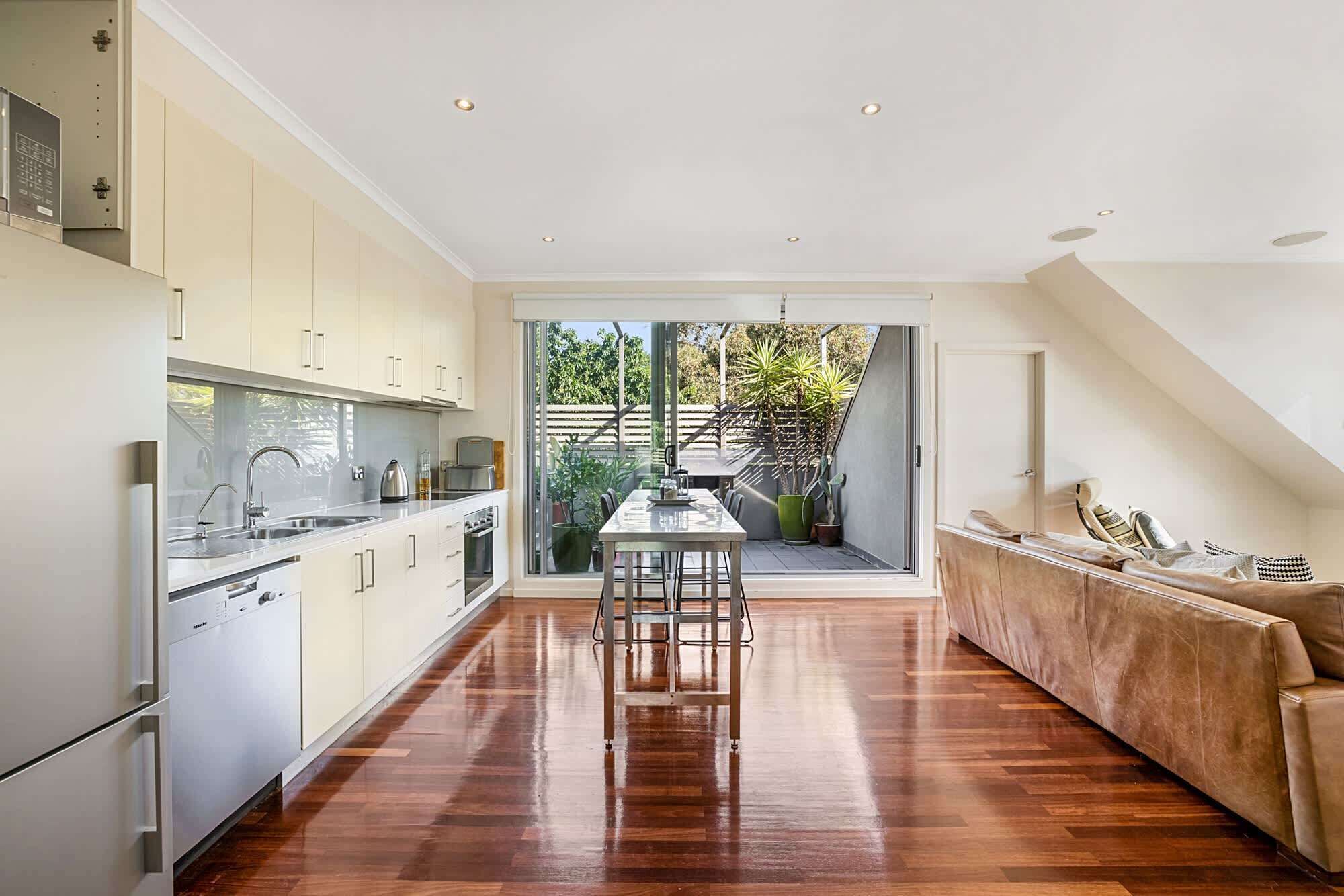 A modern kitchen with a dining area, a sofa, and a view of the outdoors.