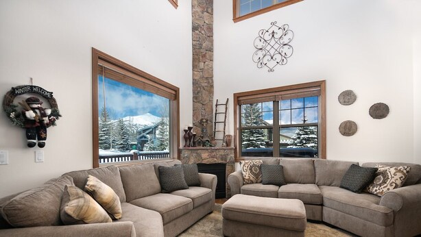 Una sala de estar acogedora con chimenea de piedra, ventanas amplias con vistas nevadas y un adorno de 'Winter Welcome'.
