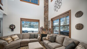 Una sala de estar acogedora con un sofá modular, una chimenea y ventanas amplias que dan a un paisaje nevado.
