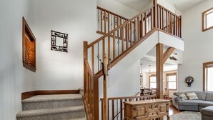 Una escalera con barandas de madera que lleva a un piso superior, un comedor con mesa y sillas de madera, y una sala de estar con un sofá gris.
