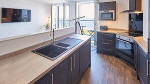 A modern kitchen with a large island, built-in oven, microwave, and a view of the sea through large windows. - Host & Stay | The Waves (Whitby)