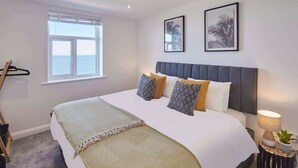 A bedroom with a large bed, a window with a view, and a bedside table with a lamp and a plant. - Host & Stay | The Waves (Whitby)