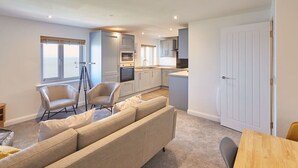 A modern kitchen with built-in appliances, a dining area with a wooden table, and a seating area with a sofa and chairs.