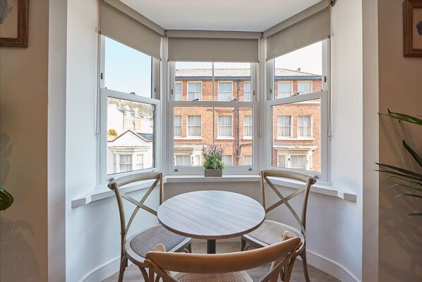 A corner room with a bay window, a round wooden table, and four wicker chairs.