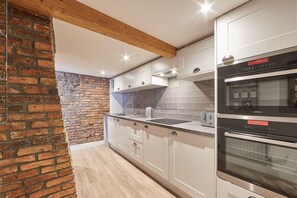 A modern kitchen with white cabinets, a brick wall, and two ovens. - Host & Stay | Othala @ The Merchants Quarters (Scarborough)