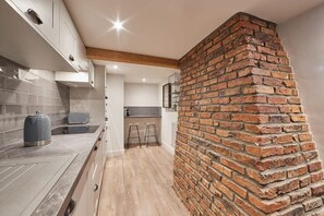A modern kitchen with a brick accent wall, wooden beams, and a tiled backsplash. - Host & Stay | Othala @ The Merchants Quarters (Scarborough)