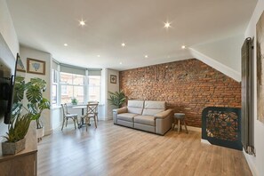 A spacious living area with a brick wall, a sofa, a dining table with chairs, and potted plants. - Host & Stay | Othala @ The Merchants Quarters (Scarborough)