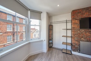 A room with a large window, a brick wall, and a metal shelf unit. - Host & Stay | Othala @ The Merchants Quarters (Scarborough)