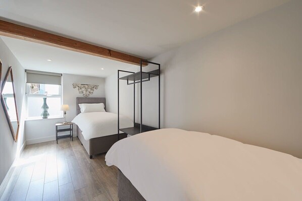 A bedroom with a large bed, a smaller bed, a nightstand, a lamp, and a window with blinds. - Host & Stay | Othala @ The Merchants Quarters (Scarborough)