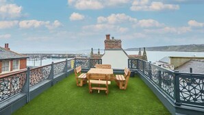 Eine Dachterrasse mit Holztisch und -stühlen, einem Zierkamin und Blick auf das Meer und die Bebauung.