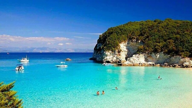 Un paysage côtier avec une eau turquoise et limpide, des bateaux et une falaise rocheuse parsemée de végétation.