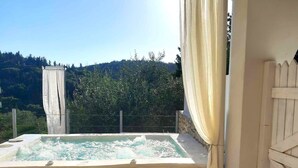 Un bain à remous avec un mur en pierre et une clôture en bois, entouré de verdure et sous un ciel dégagé.