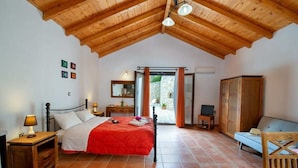 Une chambre avec un plafond en bois, un lit recouvert d’une couverture rouge, une table de chevet, une armoire et une vue sur l’extérieur.