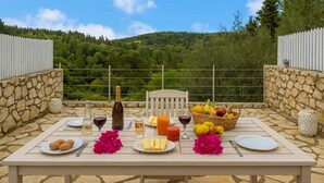 Een buitentafel gedekt met eten en drinken, omgeven door stenen muren en een prachtig uitzicht op heuvels.