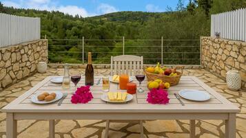 Enjoy a meal al fresco in this serene outdoor dining area, surrounded by lush greenery and a charming stone wall.